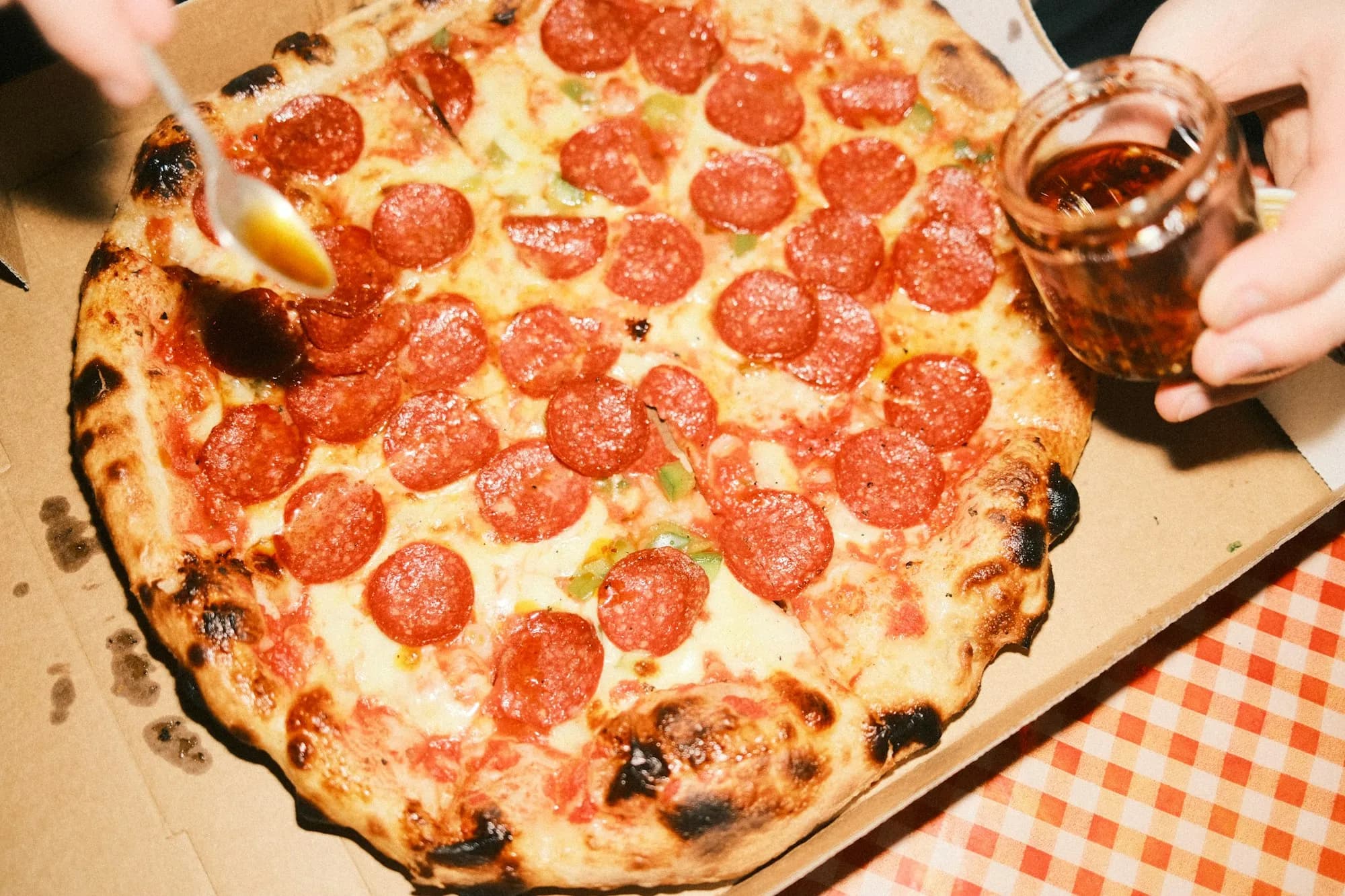 Pizza de embutido curado rojo con miel cayendo de una cuchara sobre la masa