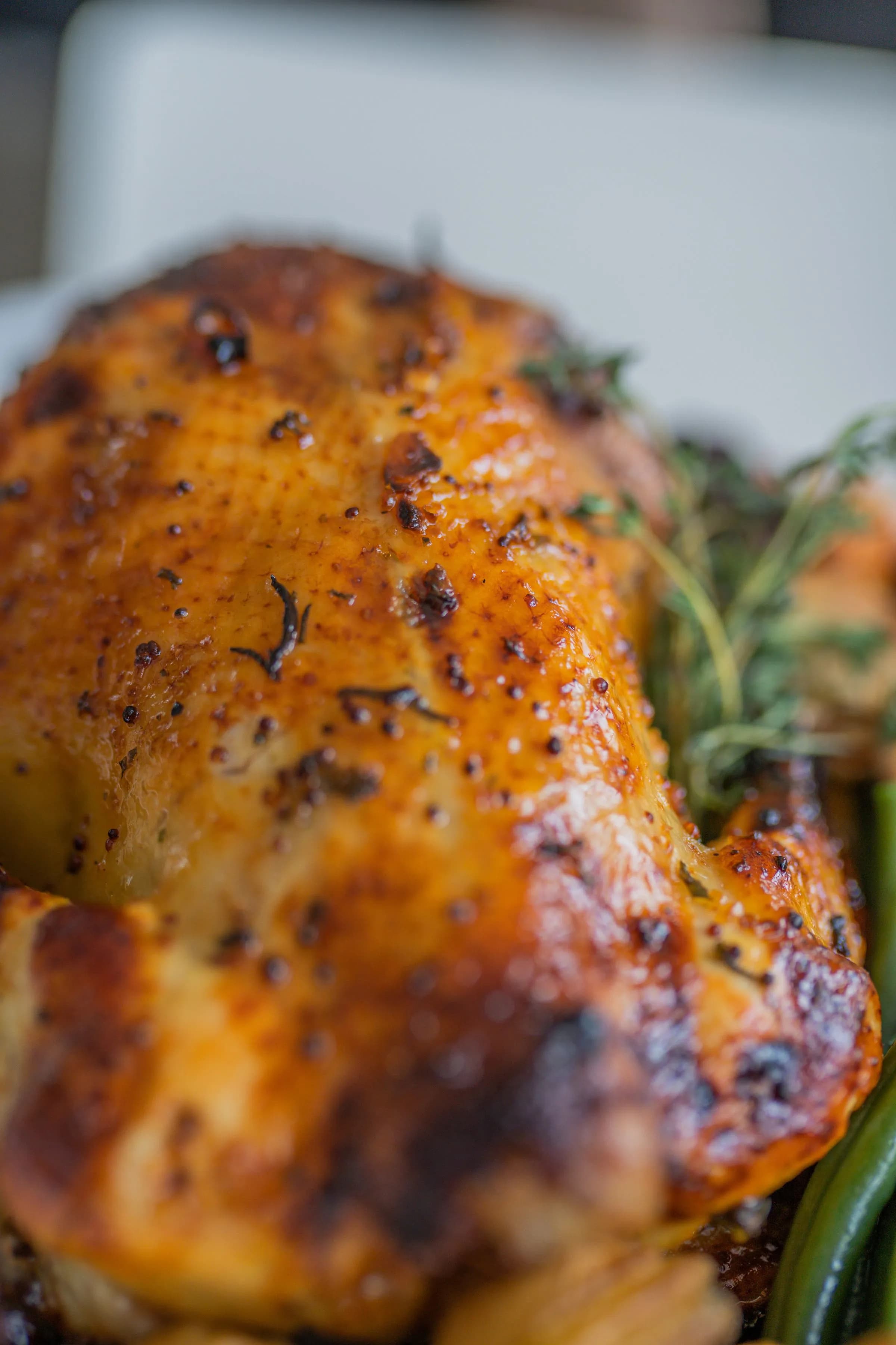 Primer plano de un pollo entero asado, de piel dorada y brillante, con ramas de hierbas