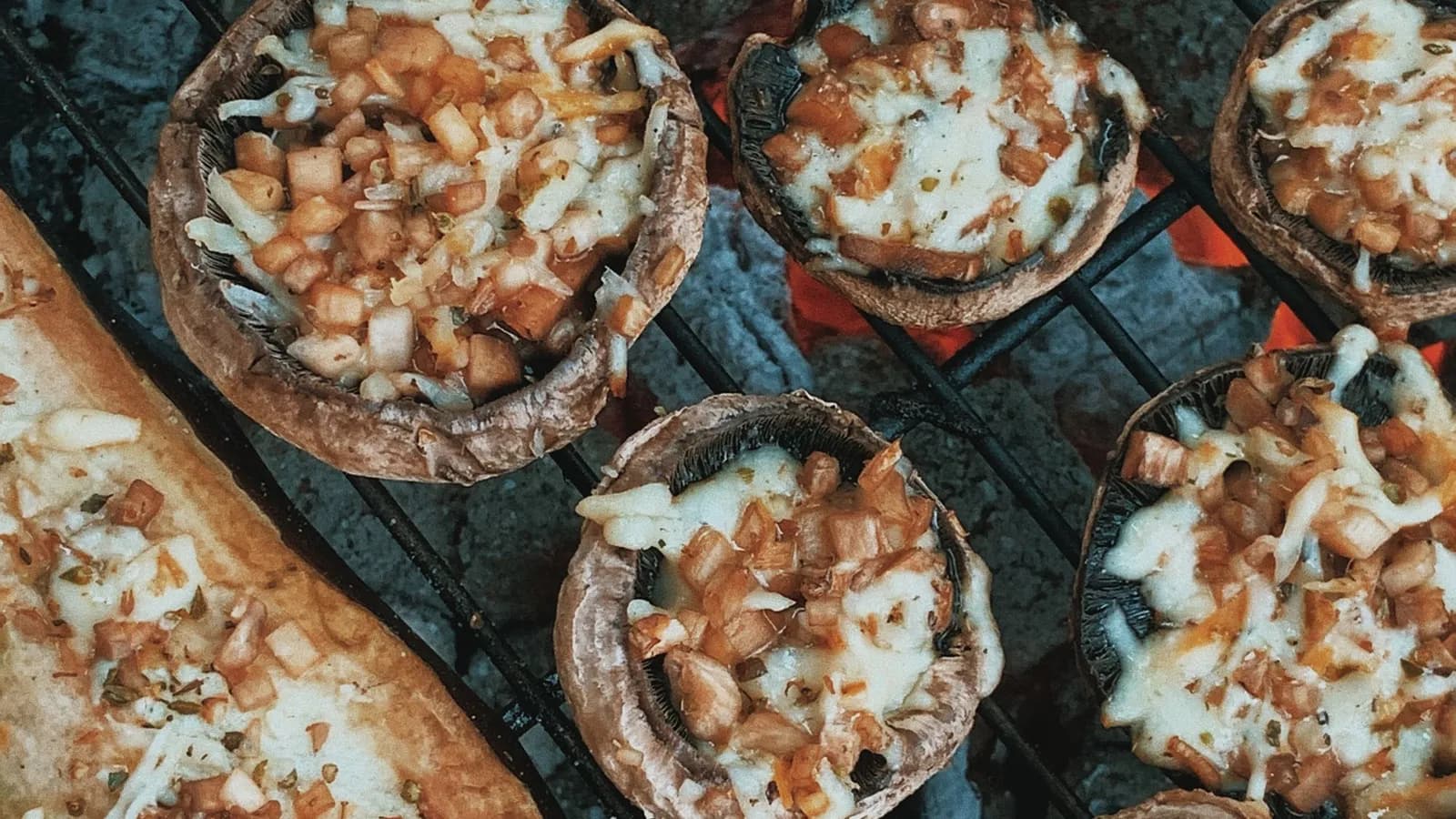 Champiñones Portobello rellenos al ajillo con pan rallado y perejil, recién gratinados y dorados sobre una plancha de hierro fundido junto a un kamado de cerámica.