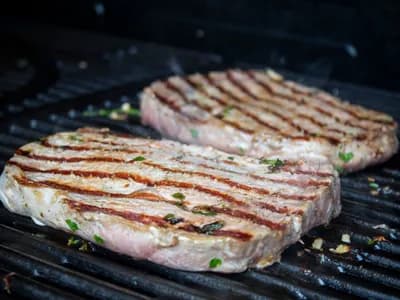 Dos filetes de presa de cerdo veteados con marcas de parrilla sobre la rejilla, fondo oscuro