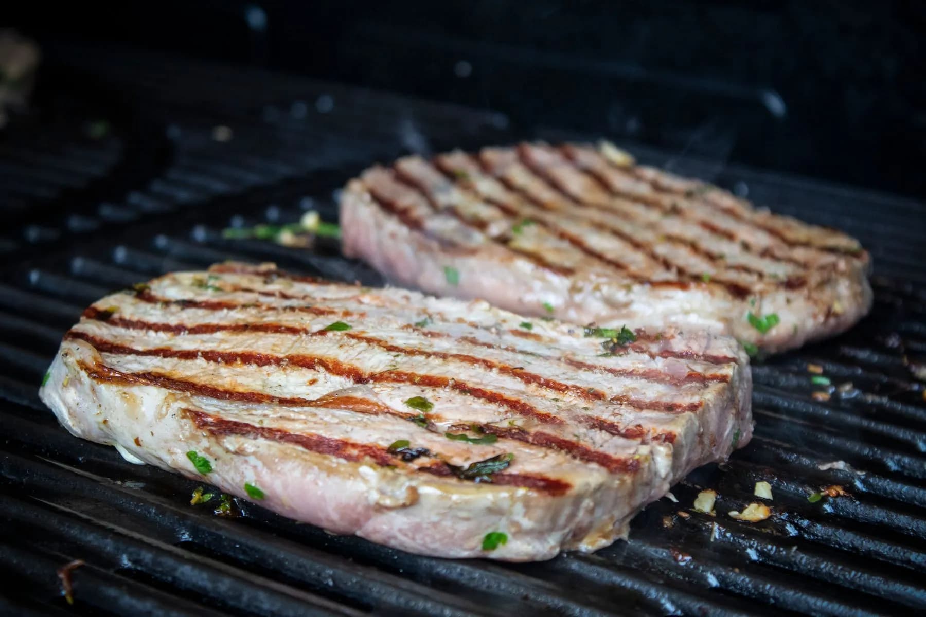 Dos filetes de presa de cerdo veteados con marcas de parrilla sobre la rejilla, fondo oscuro