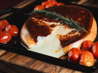 Rueda de provolone fundido a la brasa en sartén de hierro fundido con tomates cherry asados y una ramita de romero