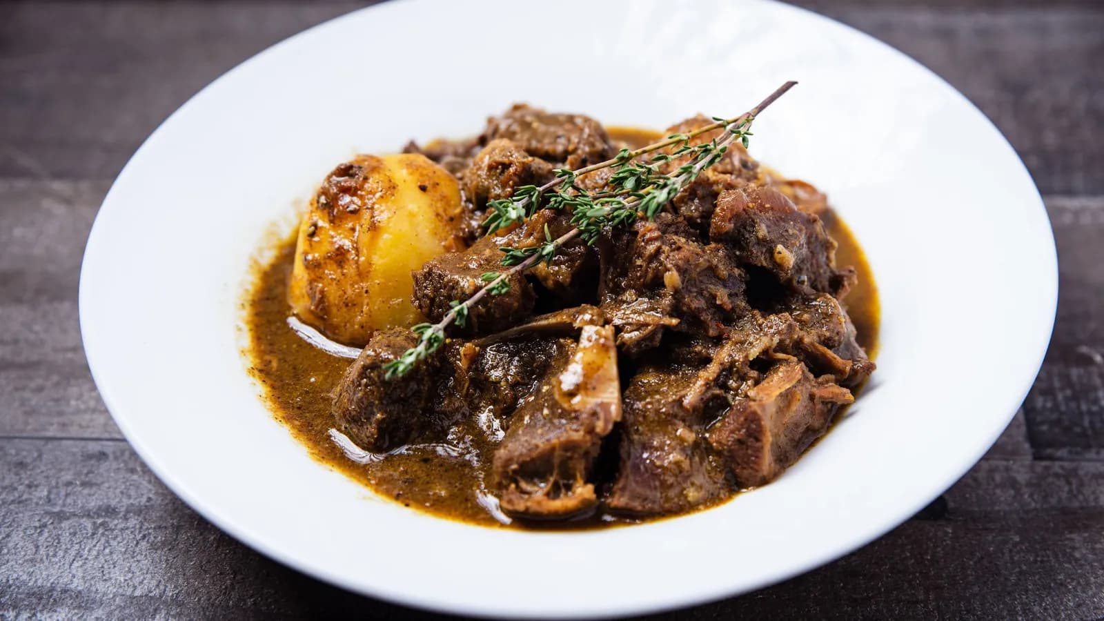Rabo estofado en salsa oscura con patata, servido en un plato hondo blanco