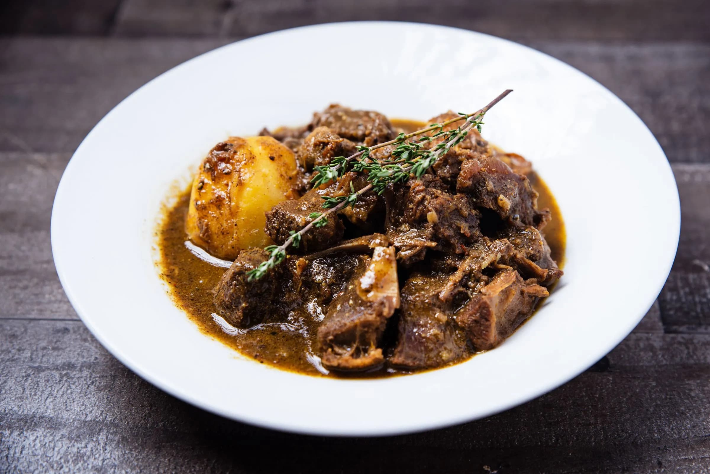 Rabo estofado en salsa oscura con patata, servido en un plato hondo blanco