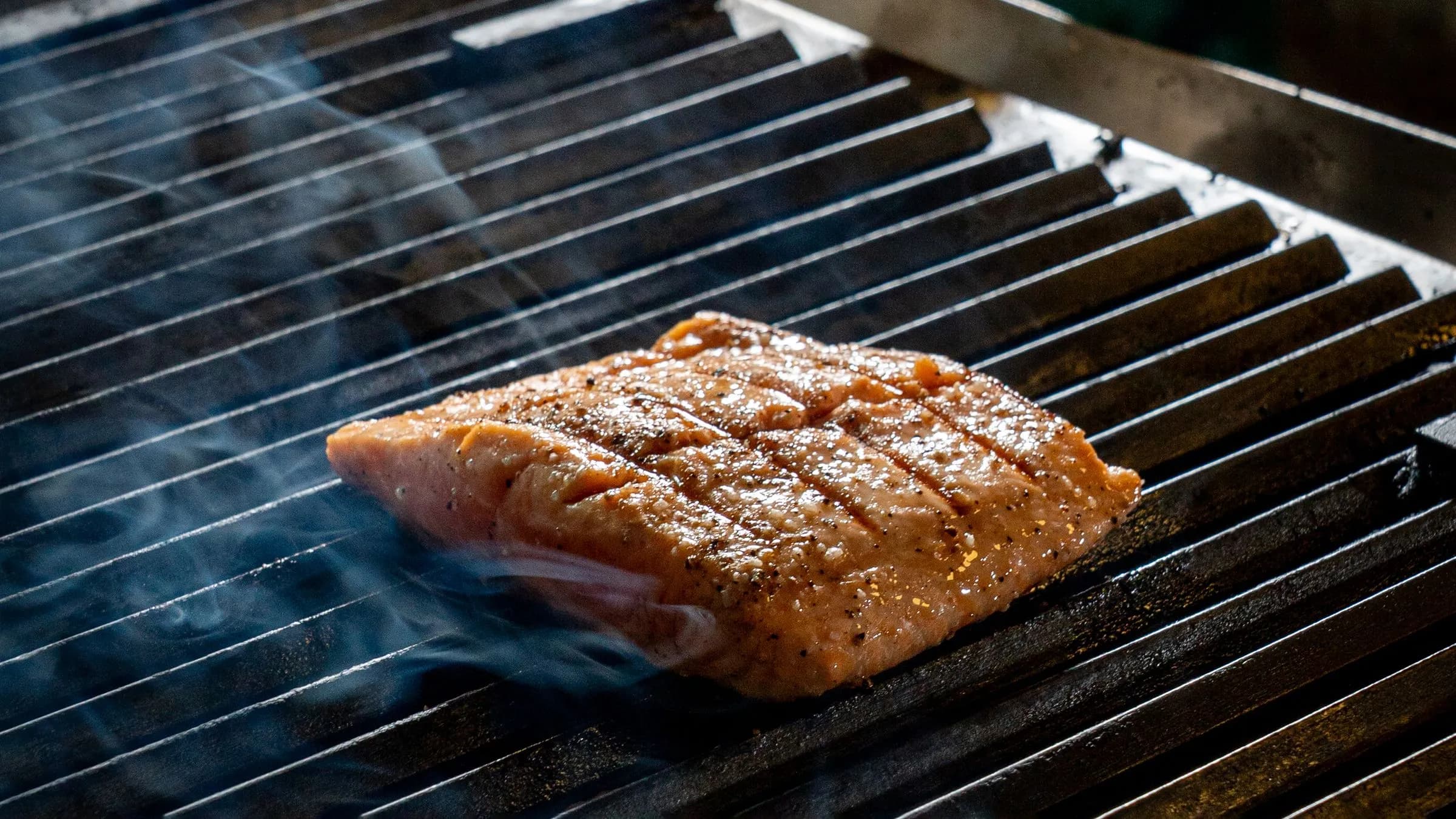 Salmon fillet with grill marks on the grate, wreathed in smoke