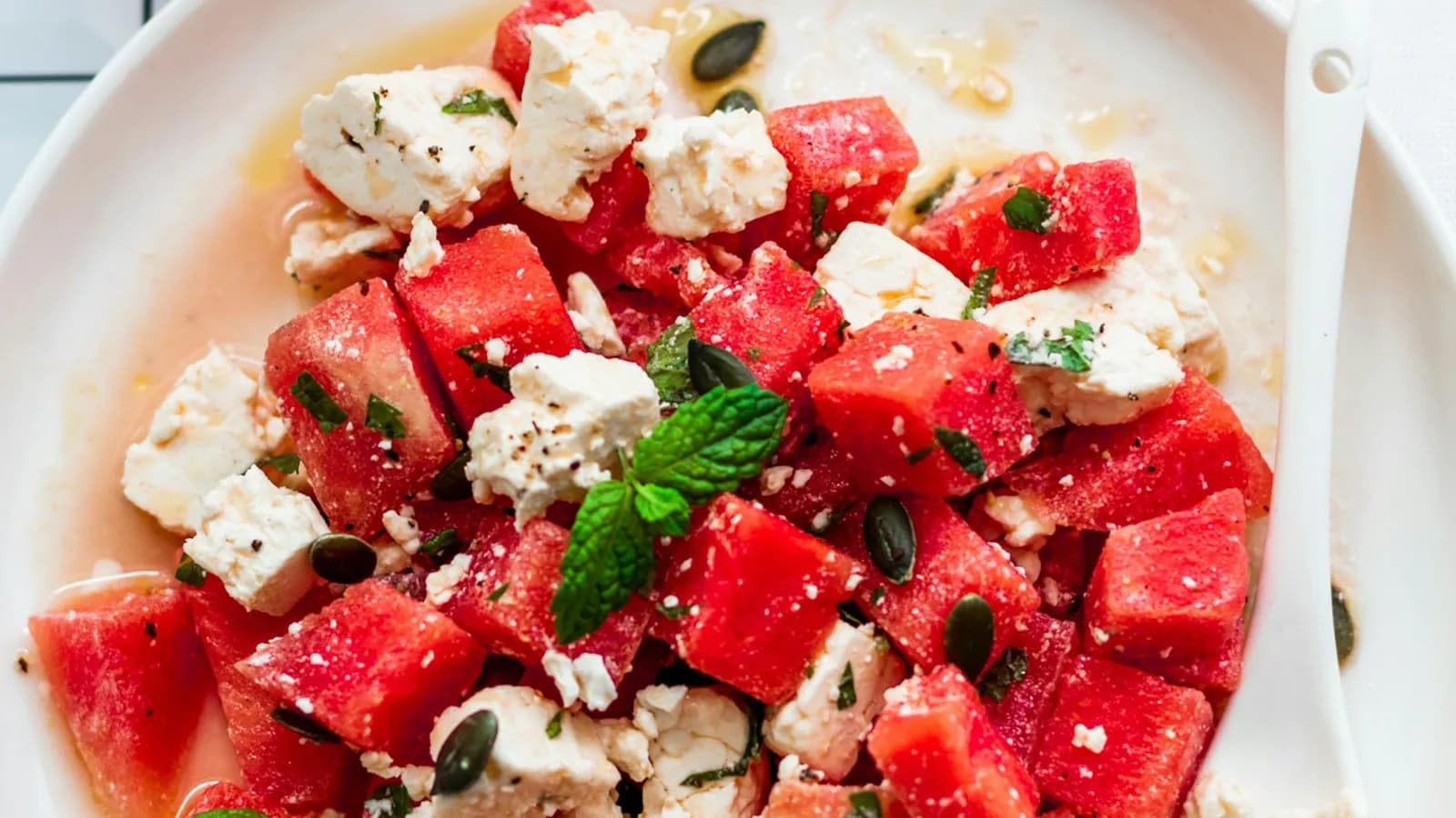 Triángulos de sandía con marcas de parrilla, feta desmenuzado, hojas de menta e hilos de reducción de balsámico sobre una tabla de roble junto a un kamado encendido.