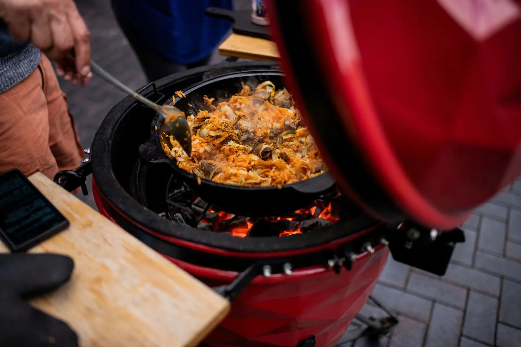 Kamado cerámico rojo con la cúpula abierta y una cazuela dentro, sobre las brasas