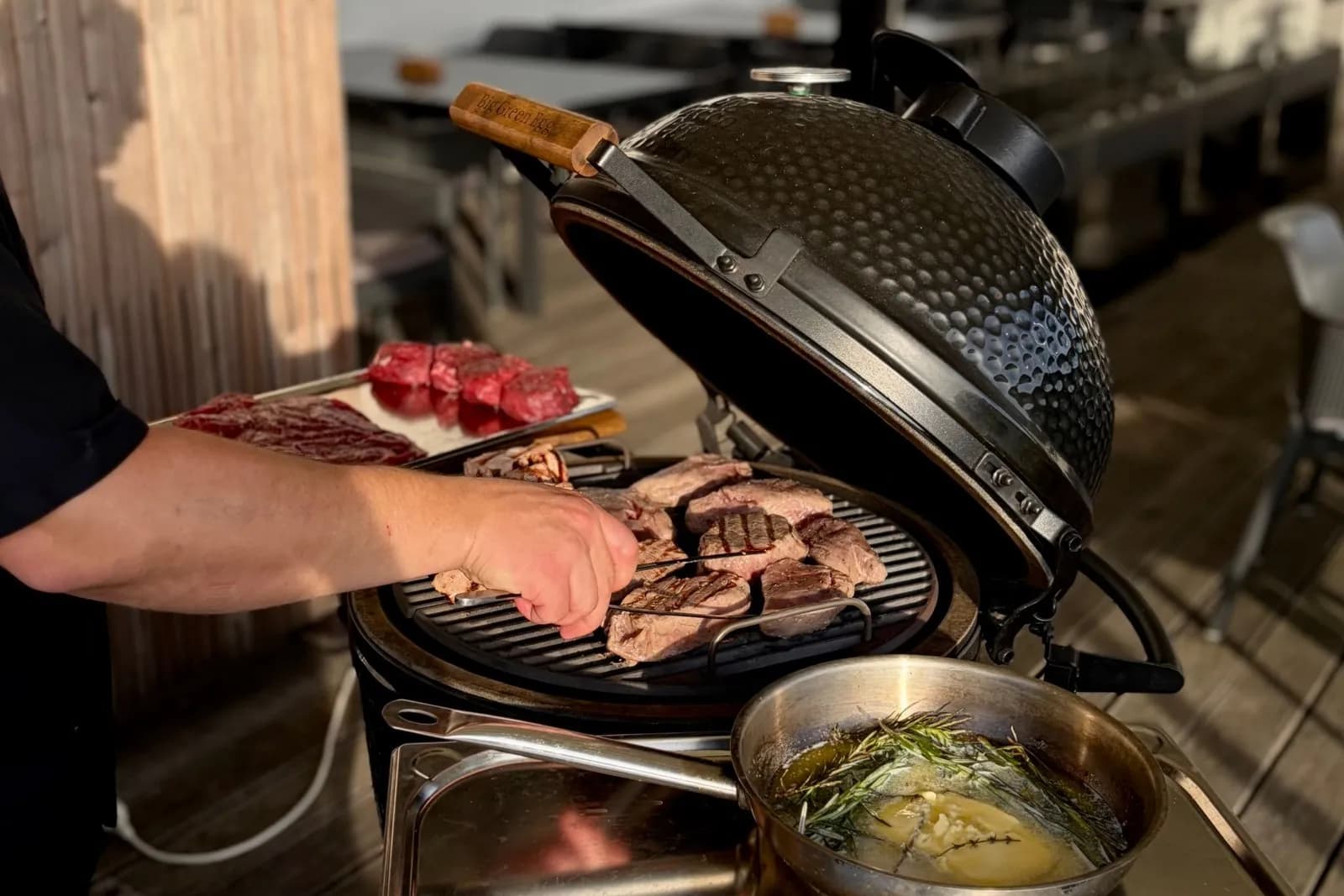 Big Green Egg MiniMax con la tapa abierta y filetes en la parrilla, en la terraza de madera de una tienda de barbacoas