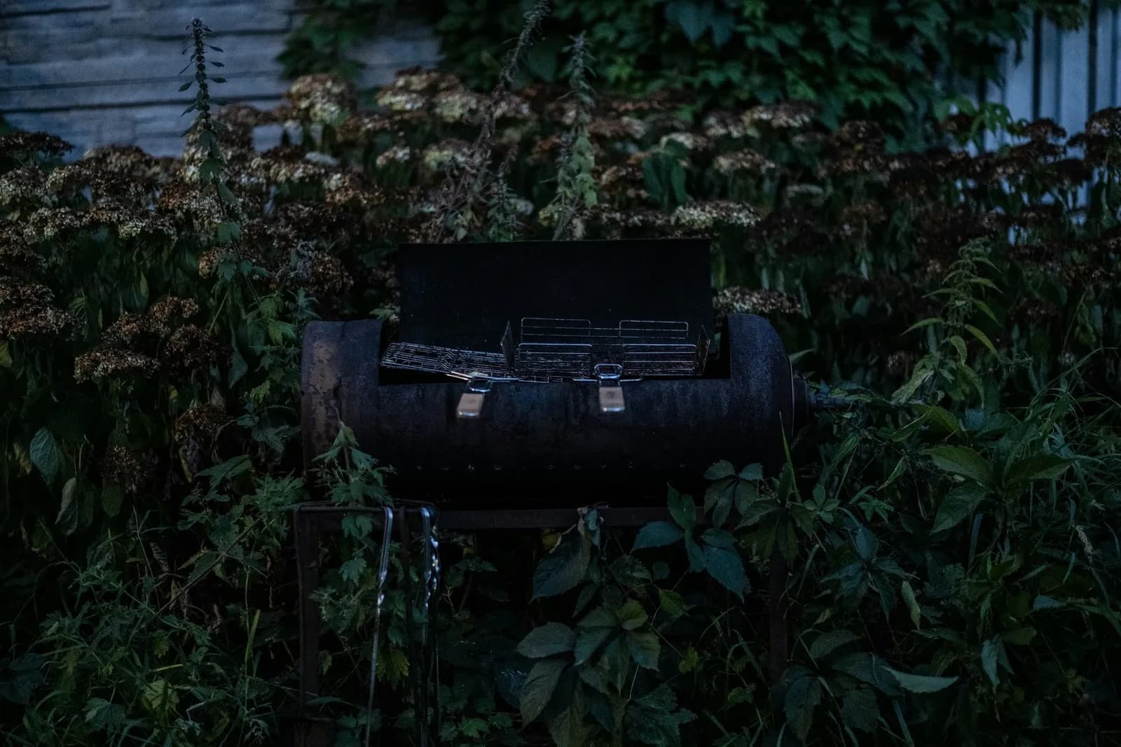 Barbacoa de barril antigua y oxidada abandonada entre la vegetación de un jardín