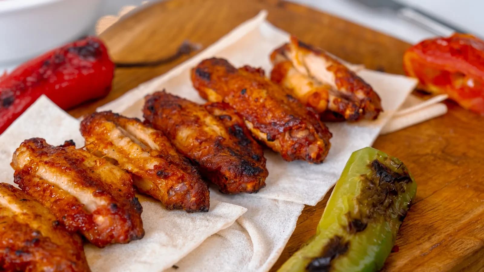 Alitas de pollo glaseadas y doradas sobre una tabla de madera con pimientos asados y guindilla