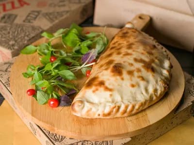 Calzone dorado y sellado sobre tabla de madera con hojas de albahaca