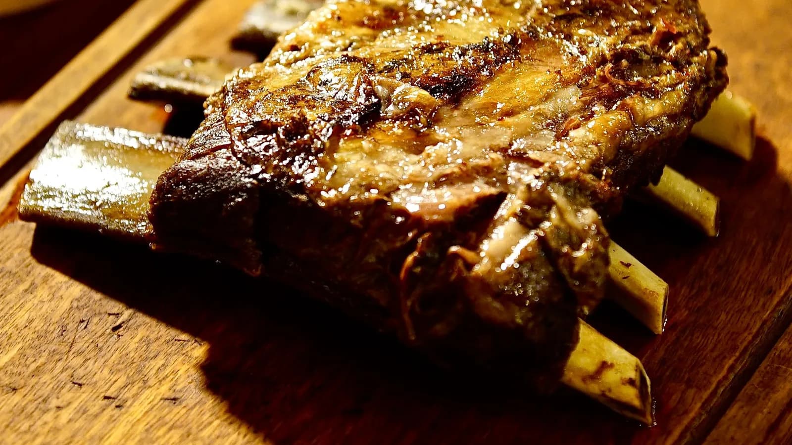 Costillar de vaca asado con la carne oscura sobre los huesos, en una tabla de madera