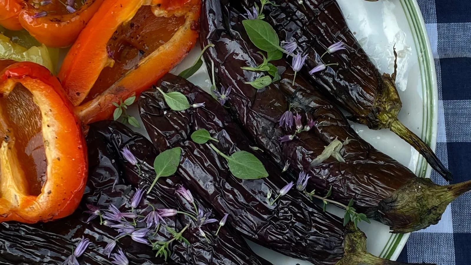 Escalivada de pimientos rojos y berenjenas asados al kamado, pelados y brillantes de aceite de oliva, con hierbas frescas por encima.