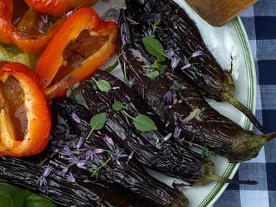 Escalivada de pimientos rojos y berenjenas asados al kamado, pelados y brillantes de aceite de oliva, con hierbas frescas por encima.