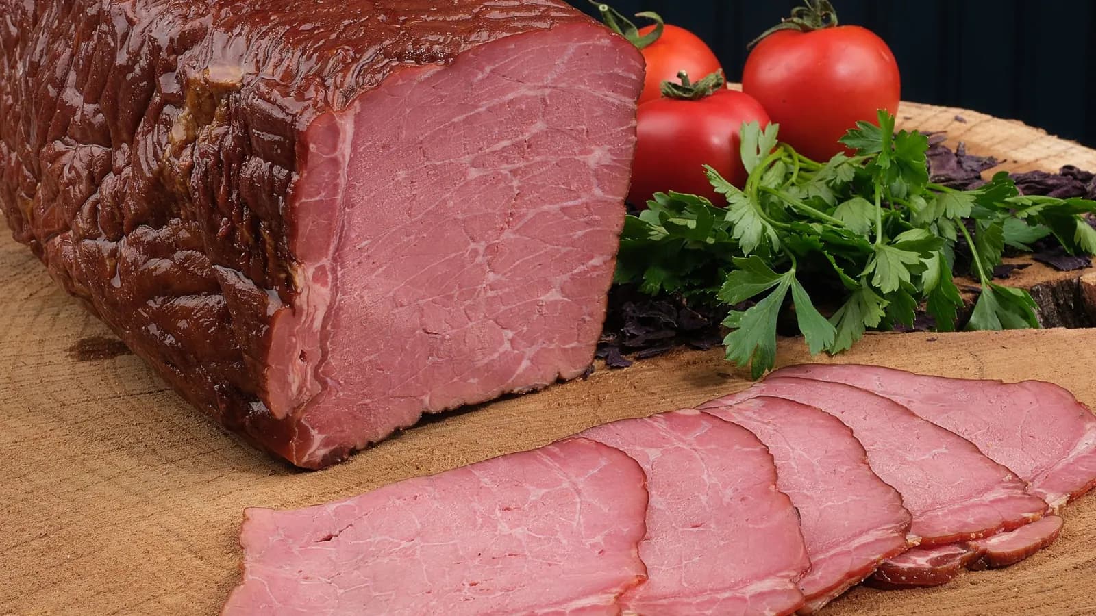 Pieza de pastrami ahumado con corteza oscura y lonchas rosadas sobre tabla de madera