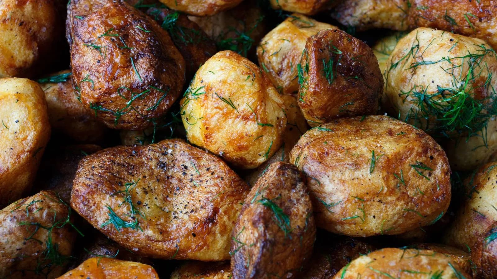Primer plano de patatas asadas de piel dorada y tostada, espolvoreadas con romero picado y pimienta negra