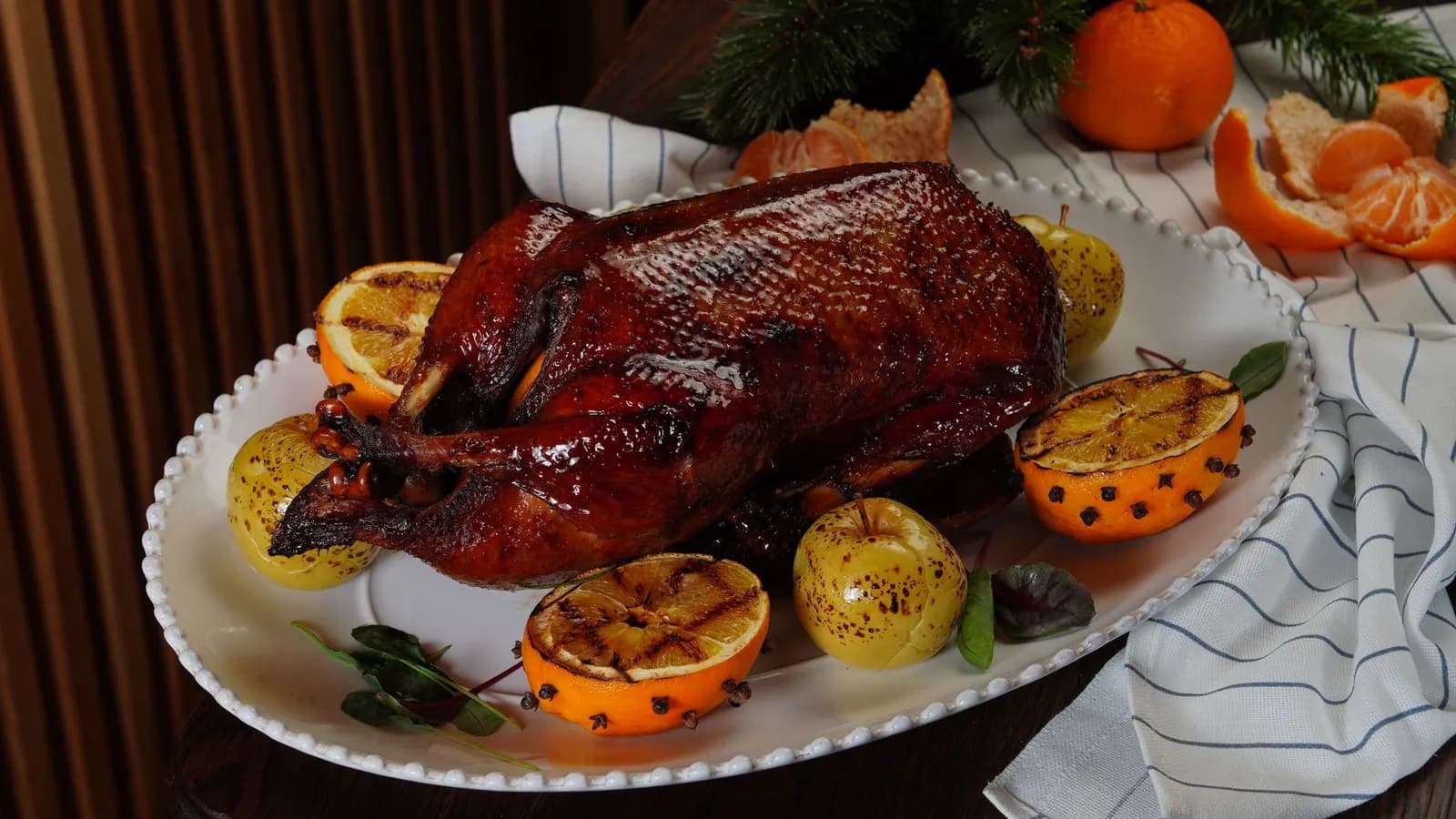 Pato entero asado con piel lacada, manzanas asadas y medias naranjas a la parrilla con clavo