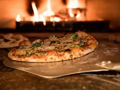 Pizza de masa madre con corteza leopardada saliendo del horno de leña