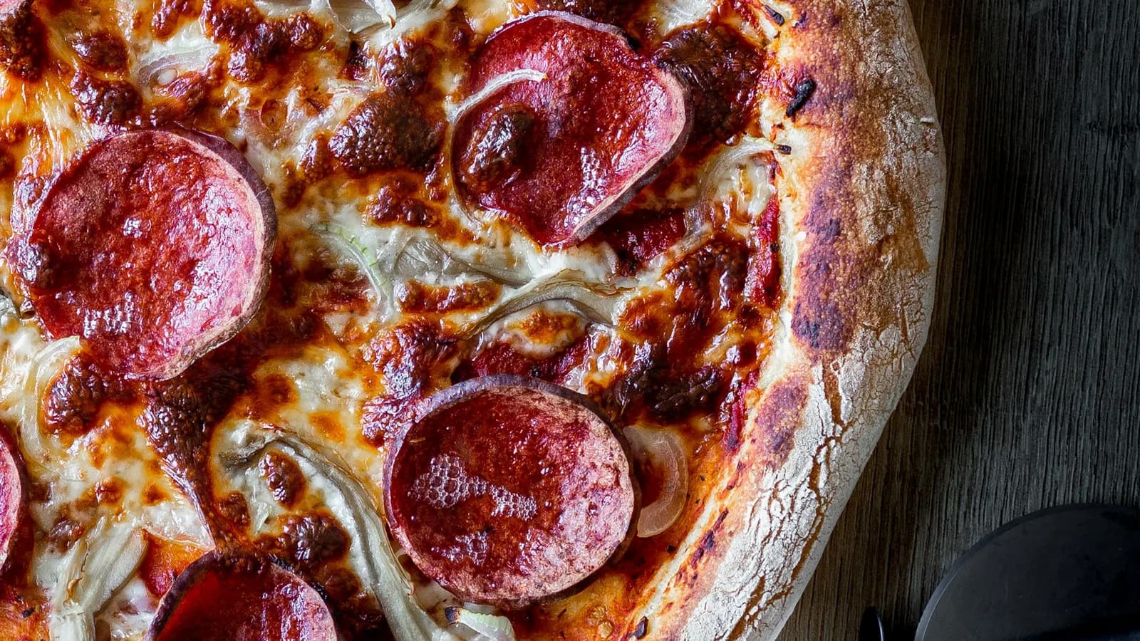 Pizza diavola con salami picante y cebolla roja, borde carbonizado de horno de leña