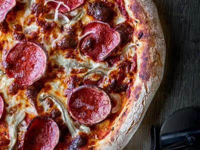 Pizza diavola con salami picante y cebolla roja, borde carbonizado de horno de leña