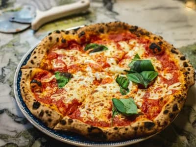 Pizza margherita con albahaca fresca y cornicione moteado, recién salida del kamado
