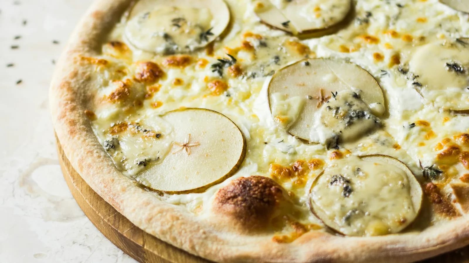 Pizza quattro formaggi blanca con gorgonzola y láminas de pera sobre mármol