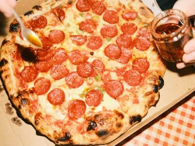 Pizza de embutido curado rojo con miel cayendo de una cuchara sobre la masa