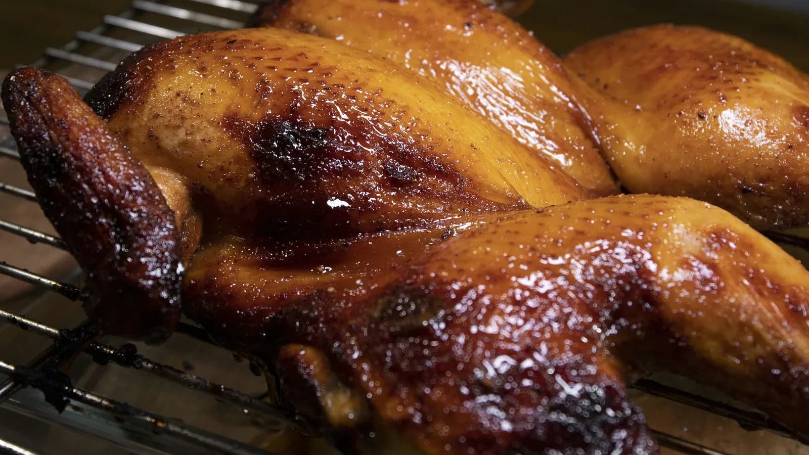 Pollo entero abierto en mariposa (spatchcock) asado al kamado, con la piel dorada y lacada, sobre rejilla de acero