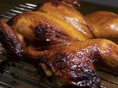 Pollo entero abierto en mariposa (spatchcock) asado al kamado, con la piel dorada y lacada, sobre rejilla de acero
