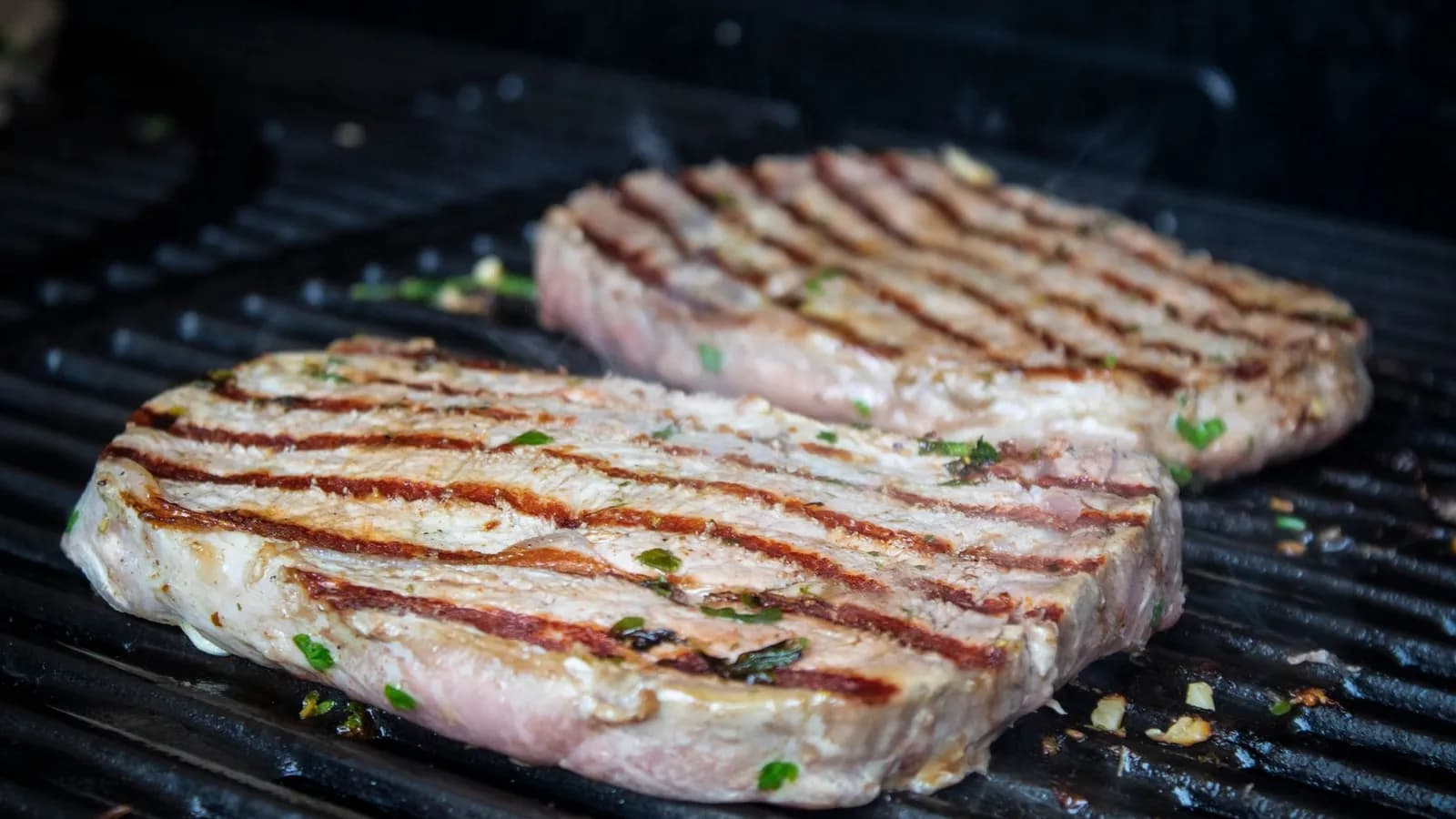 Dos filetes de presa de cerdo veteados con marcas de parrilla sobre la rejilla, fondo oscuro