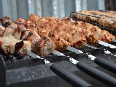 Brochetas de cuello de cerdo doradas sobre pinchos metálicos, asándose sobre las brasas
